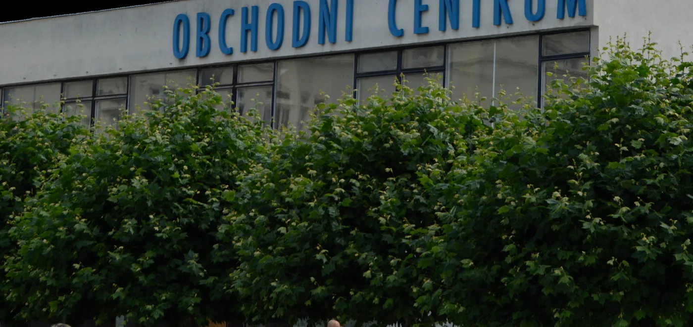 Nápis OBCHODNÍ CENTRUM na průčelí Slezanky, před budovou vzrostlé keře.