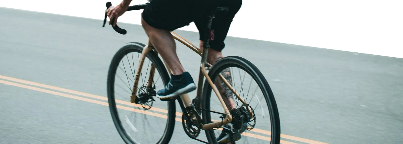Cyklista s batohem na zádech jedoucí po silnici, pohled zezadu.