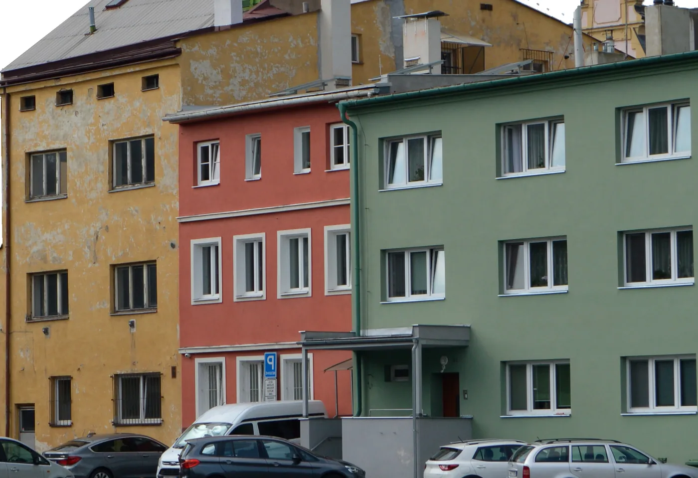 Řada opavských činžovních domů se žlutou, červenou a zelenou fasádou, před nimi zaparkovaná auta.